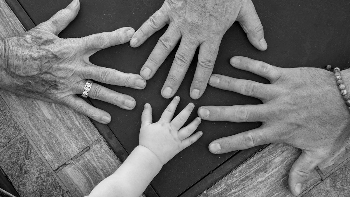 Four hands of different ages reaching towards center